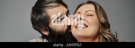 Un couple en tenue élégante partage un moment tendre, la femme riant tandis que son partenaire se penche pour un baiser. Banque D'Images