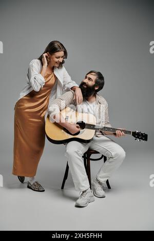 Un homme et une femme posent ensemble dans un studio. Il joue de la guitare acoustique pendant qu'elle se tient à côté de lui. Banque D'Images