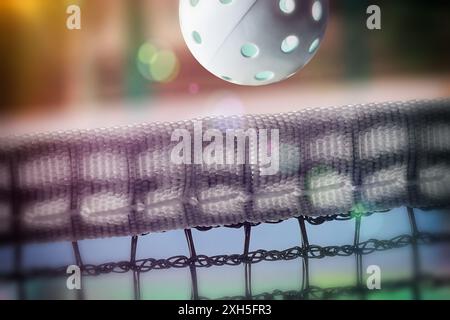 Fond sportif avec balle de pickleball traversant le filet sur un terrain de jeu. Vue latérale. Banque D'Images