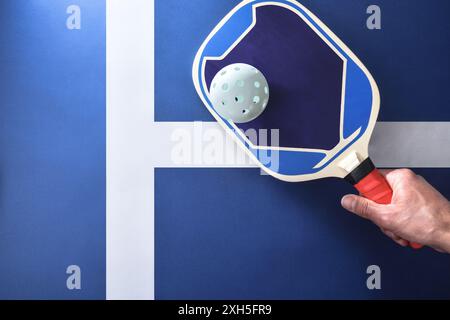 Main avec pagaie bleue de pickleball frappant une balle blanche sur la surface de jeu. Vue de dessus. Banque D'Images