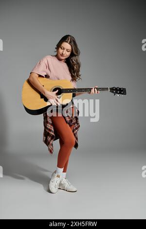 Une jeune femme en tenue élégante strums une guitare acoustique avec passion. Banque D'Images