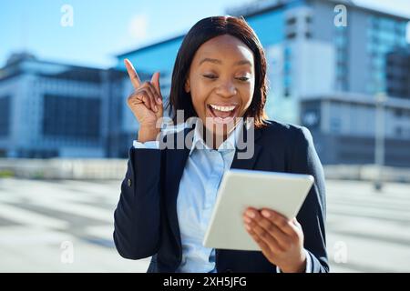 Femme d'affaires afro-américaine excitée utilisant la tablette dans un cadre urbain Banque D'Images