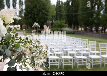 Les chaises blanches disposées en rangées sur la pelouse sont décorées de fleurs pour une cérémonie de mariage en plein air Banque D'Images