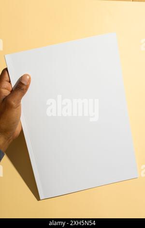Homme biracial tenant un papier blanc vierge, avec espace de copie. Idéal pour les présentations ou la publicité dans un contexte propre et simple. Banque D'Images