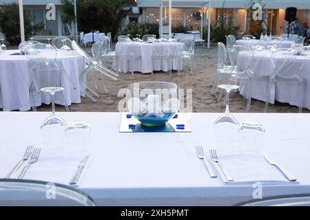 Tables rondes avec nappes blanches et chaises transparentes mises en place pour un événement sur la plage Banque D'Images