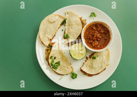 Four tacos with salsa and lime on a white plate on green background Stock Photo