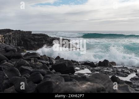 Ocean waves crash onto black lava rock along seawall in Kailua-Kona. Stock Photo