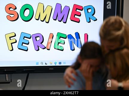 Wiesbaden, Allemagne. 12 juillet 2024. Devant un tableau blanc sur lequel sont inscrites les mots 'vacances d'été', le professeur d'une classe de 4e année de l'école primaire Robert Schumann dit au revoir à deux enfants le dernier jour de l'école. Les vacances d'été commencent aujourd'hui pour environ 850 000 élèves en Hesse. Crédit : Arne Dedert/dpa/Alamy Live News Banque D'Images