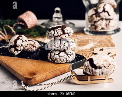 Un gros plan de biscuits de noël craquelés empilés sur une planche de bois avec des décorations festives en arrière-plan. Banque D'Images