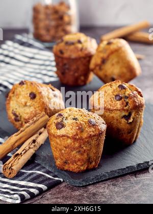 Un gros plan d'un cupcake aux pépites de chocolat fraîchement végétalien à la banane sur une planche d'ardoise avec des bâtons de cannelle et des amandes dans un bocal en arrière-plan. Banque D'Images