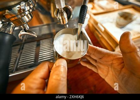 Gros plan sur les mains du barista moussant du lait chaud sur une machine à café Banque D'Images