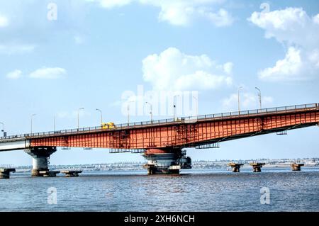 Un camion jaune traversant un grand pont rouge sur une rivière calme. Mykolaiv, Ukraine Banque D'Images