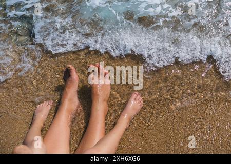 Les pieds de la mère et du fils sont positionnés près les uns des autres sur le rivage de l'océan Banque D'Images