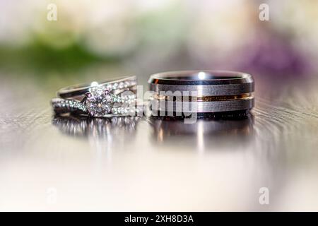 Mariée et mariée anneaux de mariage sur la surface réfléchissante avec fond bokeh rose et vert Banque D'Images