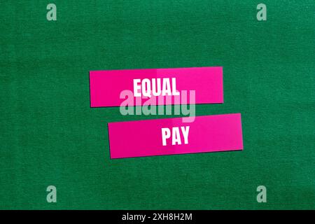 Message d'égalité salariale écrit sur du papier rose avec fond vert. Symbole conceptuel de l'égalité salariale. Copier l'espace. Banque D'Images