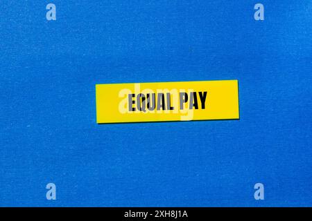 Message d'égalité salariale écrit sur du papier jaune sur fond bleu. Symbole conceptuel de l'égalité salariale. Copier l'espace. Banque D'Images