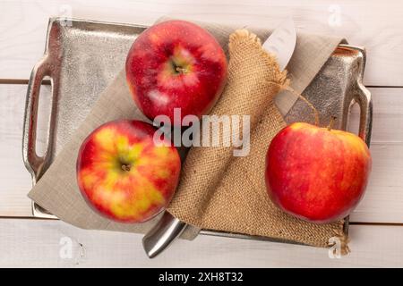 Trois pommes rouges avec couteau et plateau en métal sur table en bois, macro, vue de dessus. Banque D'Images