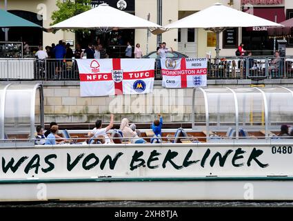 Les fans d'Angleterre sur Friedrichstrasse drapent des drapeaux près de la rivière Spree à Berlin, en Allemagne. L'Angleterre affrontera l'Espagne dans la finale de l'UEFA Euro 2024 dimanche. Date de la photo : vendredi 12 juillet 2024. Banque D'Images