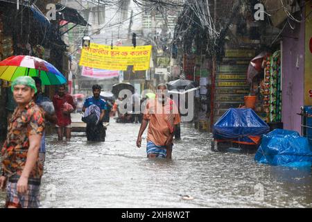 Les navetteurs traversent une route goudronnée par l'eau après de fortes pluies à Dhaka, au Bangladesh. 12 juillet 2024. Il pleut abondamment et sans arrêt à Dhaka depuis 6h00. Les routes de plusieurs quartiers de la ville ont été inondées. Il y a de l'eau à la taille dans ces routes. Les piétons souffrent énormément. Photo de Suvra Kanti Das/ABACAPRESS. COM Credit : Abaca Press/Alamy Live News Banque D'Images