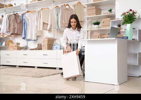 Vendeur féminin emballant des chaussures en ligne commandées dans le sac dans le magasin de vêtements Banque D'Images