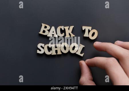 Mains arrangeant les lettres en bois orthographiant 'retour à l'école' sur fond sombre. Image conceptuelle pour l'éducation, la nouvelle année scolaire, l'apprentissage et l'école p Banque D'Images