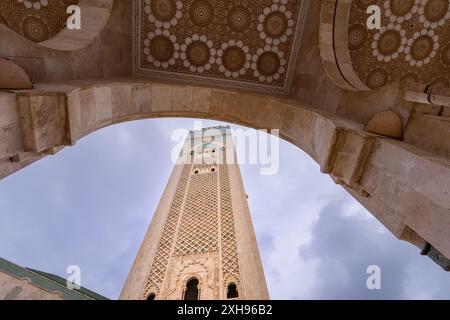 Une vue en bas angle de l'imposant minaret de la mosquée Hassan II, avec ses arches richement structurées, se détachant sur un ciel nuageux. Casablanca, M. Banque D'Images