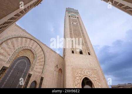 Une vue en bas angle de l'imposant minaret de la mosquée Hassan II, avec ses arches richement structurées, se détachant sur un ciel nuageux. Casablanca, M. Banque D'Images