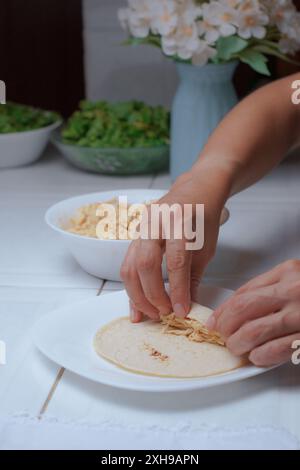 Femme chef préparant des tacos dans sa cuisine, seules ses mains sont vues rouler une tortilla pour faire de délicieux tacos mexicains, vue rapprochée. Banque D'Images