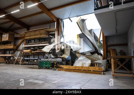 Telgte, Allemagne. 12 juillet 2024. Dans un atelier de menuiserie, des conteneurs d'une entreprise adjacente pour la construction de systèmes et de modules ont volé à travers le mur. Dégâts après une tempête violente à Telgte, Münsterland. Crédit : Guido Kirchner/dpa/Alamy Live News Banque D'Images