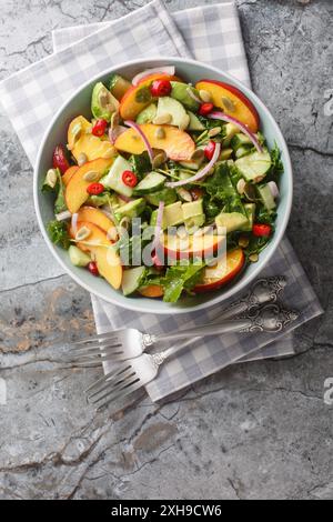 Salade végétarienne d'avocat de pêche avec oignon rouge, piment, roquette, épinards et graines de citrouille vêtues d'huile d'olive dans un bol sur la table. Verti Banque D'Images