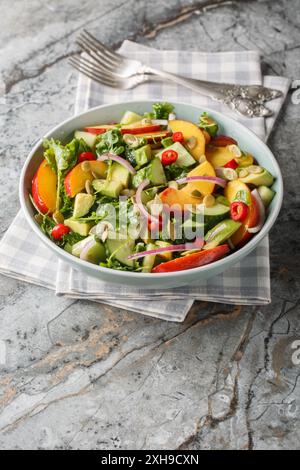 Salade végétarienne d'avocat de pêche avec oignon rouge, piment, roquette, épinards et graines de citrouille vêtues d'huile d'olive dans un bol sur la table. Verti Banque D'Images