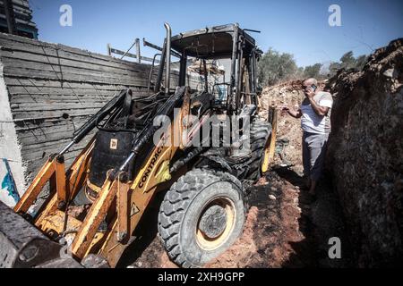 Naplouse, Palestine. 12 juillet 2024. Un palestinien inspecte un bulldozer brûlé par des colons juifs de la colonie israélienne de Homesh. Un groupe de colons masqués a attaqué des magasins et des maisons dans le village de Bazaria, au nord de la ville de Naplouse, en Cisjordanie. Crédit : SOPA images Limited/Alamy Live News Banque D'Images