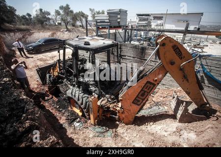 Naplouse, Palestine. 12 juillet 2024. Un palestinien inspecte un bulldozer brûlé par des colons juifs de la colonie israélienne de Homesh. Un groupe de colons masqués a attaqué des magasins et des maisons dans le village de Bazaria, au nord de la ville de Naplouse, en Cisjordanie. Crédit : SOPA images Limited/Alamy Live News Banque D'Images