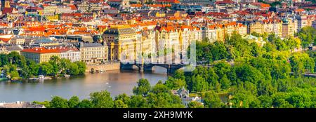 Une vue sur le Théâtre National de Prague, avec la rivière Vltava et un pont au premier plan entouré d'arbres verdoyants et une architecture classique sous un ciel clair. Prague, Tchéquie Banque D'Images