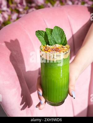 Smoothie vert rafraîchissant garni de feuilles de menthe et de flocons d'or, servi dans un grand verre. Banque D'Images