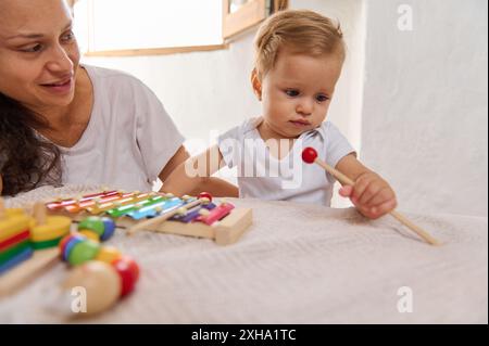 Une mère et son bébé passent du temps de qualité à jouer avec un xylophone coloré. Le bébé est concentré tandis que la mère regarde avec un sourire, mettant en vedette famil Banque D'Images