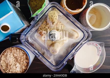 Vue aérienne des ingrédients du smoothie à la banane et à la framboise dans un mélangeur : pichet de mélangeur rempli et entouré d'ingrédients du smoothie Banque D'Images