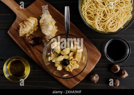 Gousses d'ail rôties avec un gousse d'ail noir : deux types de gousses d'ail dans un petit bol en verre avec un plat de spaghetti nion sur le côté Banque D'Images