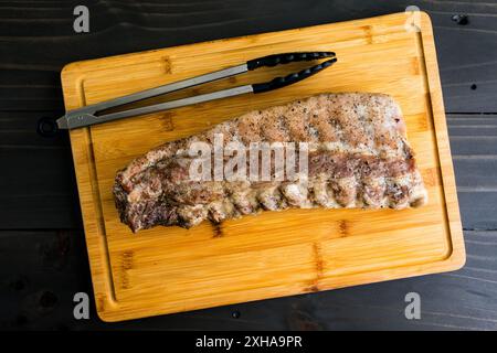 Plaque de côtes de dos rôties sur une planche à découper : plaque entière de côtes de porc sans sauce sur une planche à découper en bambou avec une paire de pinces Banque D'Images