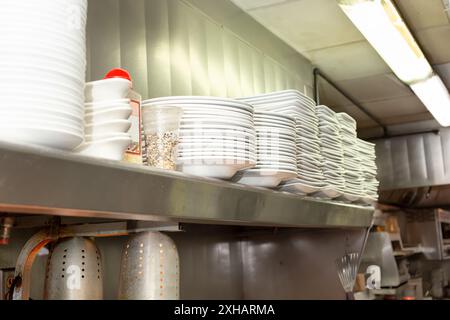 Une vue d'une étagère avec plusieurs piles d'assiettes blanches sur, dans un cadre de cuisine de restaurant. Banque D'Images