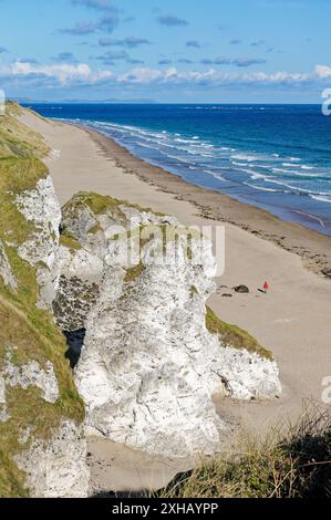 Jeune femme marcher seule sur la plage de White Rocks entre Portrush et Bushmills, Irlande du Nord. Falaises de calcaire érodé Banque D'Images