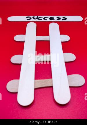 Cheminez vers le succès. Échelles en bois abstraites fabriquées à partir de bâtons Popsicle sur fond de papier rouge. Au sommet, concept. Banque D'Images