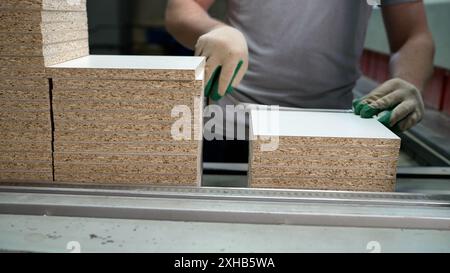 Les mains masculines travaillent sur une machine dans une usine de meubles. Les mains de menuisier prennent des ébauches pour les meubles, concept de petite entreprise. Fabrication et Banque D'Images