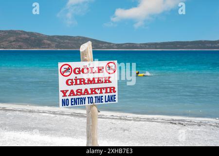 Panneau écrit en anglais et en turc sur le lac Salda : pas d'entrée au lac ( Gole Girmek Yasaktir ) et les gens nagent dans le fond Banque D'Images