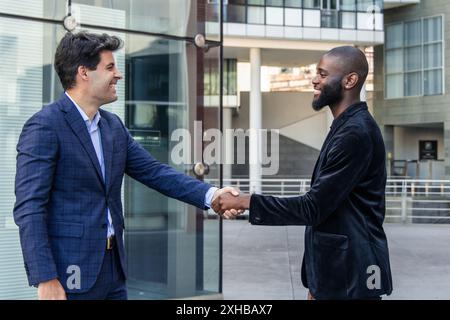 Divers professionnels, un africain et un hispanique, se saluent avec une poignée de main dans le centre financier urbain animé, mettant en valeur le di corporatif Banque D'Images