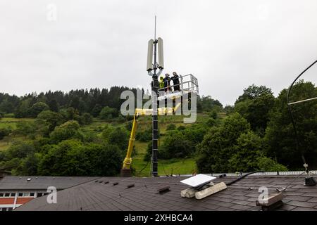 PRODUCTION - 10 juillet 2024, Bade-Württemberg, Forbach : des techniciens se tiennent sur une plate-forme élévatrice et travaillent sur un mât de téléphone portable, tandis qu'une antenne satellite Starlink blanche est visible au premier plan. Vodafone coopère avec la société américaine Starlink dans le cadre d’un projet pilote de couverture de téléphonie mobile dans les zones rurales, dont les satellites peuvent actuellement fournir un accès Internet rapide dans toute l’Europe, l’Amérique du Nord, l’Amérique du Sud et l’Australie. Le fournisseur de téléphonie mobile a installé à cet effet un mât de transmission à Forbach, qui établit le contact avec les serveurs de Vodafone à Francfort via Starlin Banque D'Images