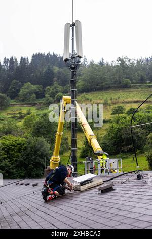 PRODUCTION - 10 juillet 2024, Bade-Württemberg, Forbach : un technicien installe une antenne satellite Starlink sur un toit, tandis que le mât de téléphone portable qui y est connecté est visible en arrière-plan. Vodafone coopère avec la société américaine Starlink dans le cadre d’un projet pilote de couverture de téléphonie mobile dans les zones rurales, dont les satellites peuvent actuellement fournir un accès Internet rapide dans toute l’Europe, l’Amérique du Nord, l’Amérique du Sud et l’Australie. Le fournisseur de téléphonie mobile a installé à cet effet un mât de transmission à Forbach, qui établit le contact avec les serveurs de Vodafone à Francfort via Starlink. Photo Banque D'Images