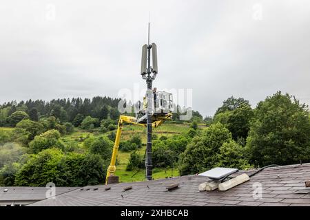 PRODUCTION - 10 juillet 2024, Bade-Württemberg, Forbach : des techniciens se tiennent sur une plate-forme élévatrice et travaillent sur un mât de téléphone portable, tandis qu'une antenne satellite Starlink blanche est visible au premier plan. Vodafone coopère avec la société américaine Starlink dans le cadre d’un projet pilote de couverture de téléphonie mobile dans les zones rurales, dont les satellites peuvent actuellement fournir un accès Internet rapide dans toute l’Europe, l’Amérique du Nord, l’Amérique du Sud et l’Australie. Le fournisseur de téléphonie mobile a installé à cet effet un mât de transmission à Forbach, qui établit le contact avec les serveurs de Vodafone à Francfort via Starlin Banque D'Images