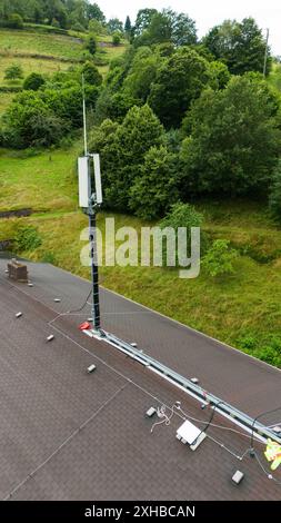 PRODUCTION - 10 juillet 2024, Bade-Württemberg, Forbach : une antenne satellite Starlink carrée est visible sur un toit à côté du mât du téléphone portable connecté via Starlink. (Photo prise avec un drone). Vodafone coopère avec la société américaine Starlink dans le cadre d’un projet pilote de couverture de téléphonie mobile dans les zones rurales, dont les satellites peuvent actuellement fournir un accès Internet rapide dans toute l’Europe, l’Amérique du Nord, l’Amérique du Sud et l’Australie. Le fournisseur de téléphonie mobile a installé à cet effet un mât de transmission à Forbach, qui établit le contact avec les serveurs de Vodafone à Francfort via Starlink. PH Banque D'Images