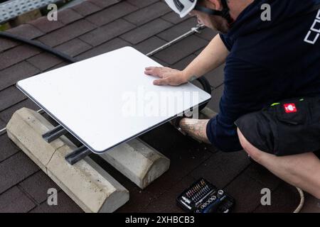 Forbach, Allemagne. 10 juillet 2024. Un technicien installe une antenne satellite Starlink sur un toit. Dans le cadre d’un projet pilote de couverture de téléphonie mobile en milieu rural, Vodafone coopère avec la société américaine Starlink, dont les satellites peuvent actuellement fournir un accès Internet rapide dans toute l’Europe, l’Amérique du Nord, l’Amérique du Sud et l’Australie. À cet effet, l'opérateur mobile a installé un mât de transmission à Forbach, qui établit le contact avec les serveurs de Vodafone à Francfort via Starlink. Crédit : Philipp von Ditfurth/dpa/Alamy Live News Banque D'Images